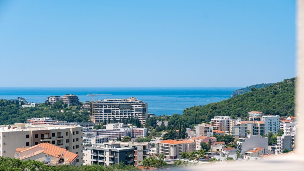 Moderna panoramska slika Bečića s pogledom na more i obližnje zgrade.